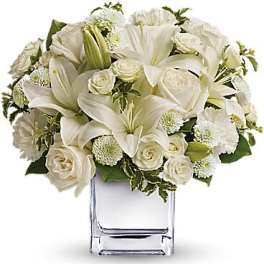 White lilies and roses arranged in a clear square vase