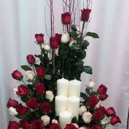 Red and white roses arranged around white pillar candles on a glass table