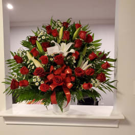 Large bouquet of red roses and white lilies in a white vase with a red ribbon