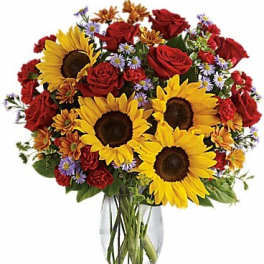 Bouquet of sunflowers, red roses, and small purple flowers in a glass vase