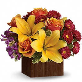 Bouquet of yellow lilies, orange roses, and red mums in a wooden cube vase
