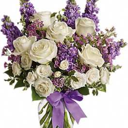 White roses and purple flowers in a clear glass vase with a purple ribbon