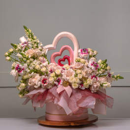 Pink and white floral arrangement in a round box with heart decorations
