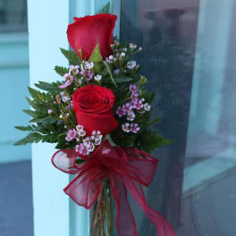 Two red roses with pink filler flowers in a glass vase