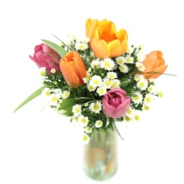 Bouquet of orange and pink tulips with white daisies in a glass vase