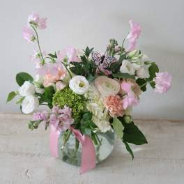 Pink and white flower arrangement in a glass vase with a pink ribbon
