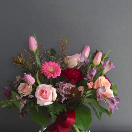 Pink roses and mixed blooms arranged in a glass vase with a red ribbon