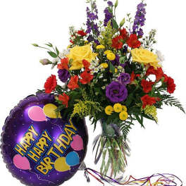 Mixed bouquet in a glass vase beside a purple happy birthday balloon.
