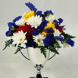 Mixed bouquet of white, yellow, red, and blue flowers in a silver trophy vase