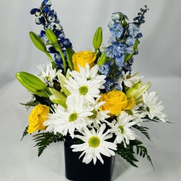Yellow roses and white daisies in a black vase with blue flowers