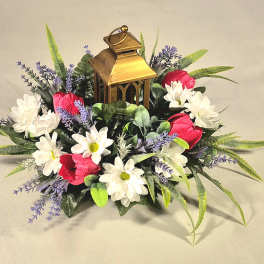 Floral arrangement with white daisies, red blooms, and a gold lantern centerpiece