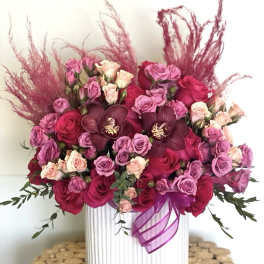 Pink and red rose arrangement in a white vase with a purple ribbon