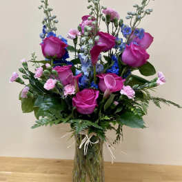 Bouquet of pink roses, blue flowers, and calla lilies in a glass vase
