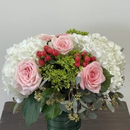 Pink roses and white hydrangeas in a glass vase with red berries