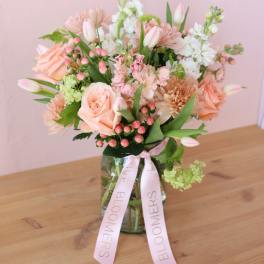 Pastel bouquet of roses, tulips, and mixed blooms in a glass vase