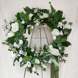 White rose and calla lily wreath on a metal stand with a green ribbon