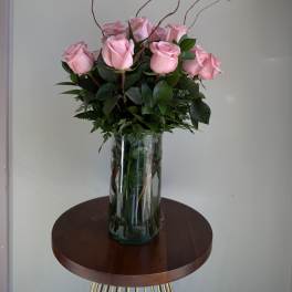 Pink roses arranged in a clear glass vase with tall curly branches