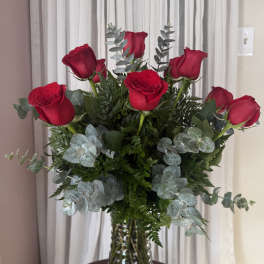 Red roses arranged in a clear glass vase with silvery eucalyptus