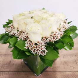 White rose bouquet in a clear glass vase with green leaves