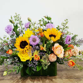 Mixed bouquet with sunflowers, roses, and purple blooms in a green vase