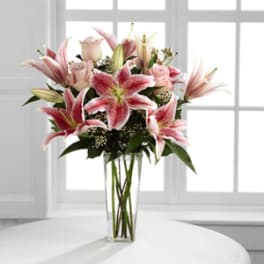 Pink lilies and roses arranged in a clear glass vase