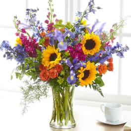 Mixed bouquet with sunflowers, purple irises, and orange roses in a glass vase