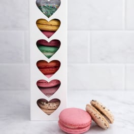 Box of assorted heart-shaped macarons with two macarons in front
