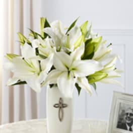 White lilies arranged in a tall white vase with a cross emblem