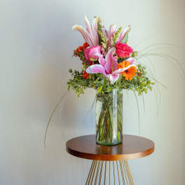 Tall bouquet of pink lilies and orange flowers in a glass vase