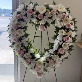 Heart-shaped standing wreath of white chrysanthemums and pale pink roses on a metal easel.