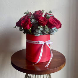 Red roses arranged in a red hat box with a white ribbon