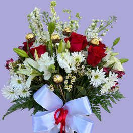 Bouquet of red roses, white lilies, and daisies in a glass vase with a ribbon