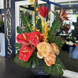 Tropical arrangement with red anthuriums, orange birds of paradise, and peach roses in a black vase