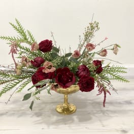 Deep red floral arrangement in a gold pedestal bowl