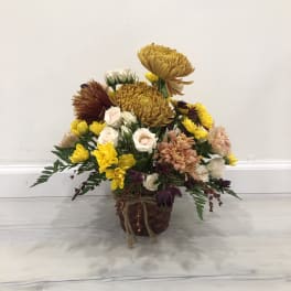 Mixed bouquet of yellow, white, pink, and burgundy flowers in a woven basket