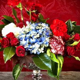 Red roses and carnations with blue hydrangeas in a silver vase