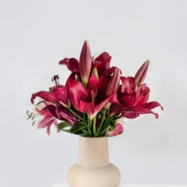 Deep pink lilies arranged in a beige vase