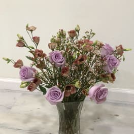 Lavender roses and small pink blooms in a clear glass vase