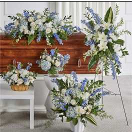 Collection of white and blue funeral flower arrangements around a wooden casket.