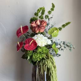 Tall floral arrangement with roses, hydrangea, and anthuriums in a glass vase