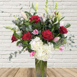 Bouquet of red roses, white hydrangea, and pink tulips in a glass vase