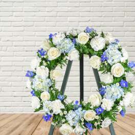Floral wreath with white roses, blue hydrangeas, and white blooms on an easel