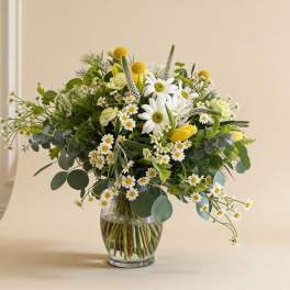 Vase arrangement of white daisies, yellow tulips, and mixed white and yellow blooms in a clear glass vase