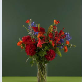 Tall mixed bouquet in a clear glass vase with red, orange, and blue flowers