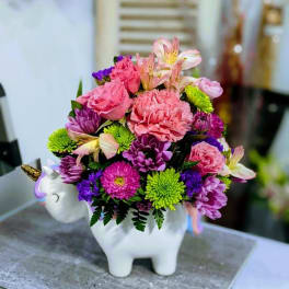Pink and purple flowers arranged in a white unicorn planter