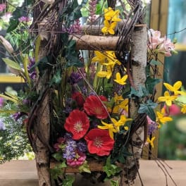 Rustic floral arrangement in a twig basket with red, yellow, and purple blooms