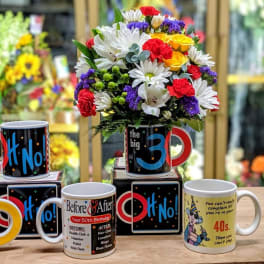 Colorful mixed flower bouquet in a mug-shaped container with novelty birthday mugs nearby