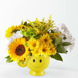 Yellow and white flower arrangement in a smiley-face mug