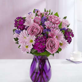 Lavender and purple mixed bouquet with roses and daisies in a purple glass vase