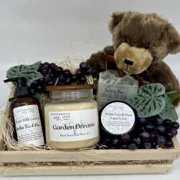 Gift basket with a teddy bear, candles, soap, lotion, scrub, and faux grapes